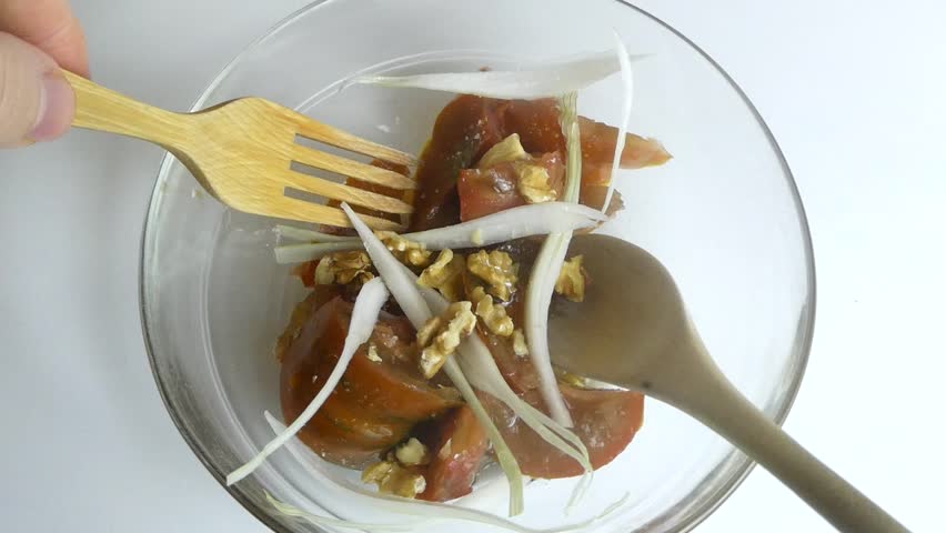 Person mixing a fresh vegetable salad with onion and walnuts using a wooden spoon and fork