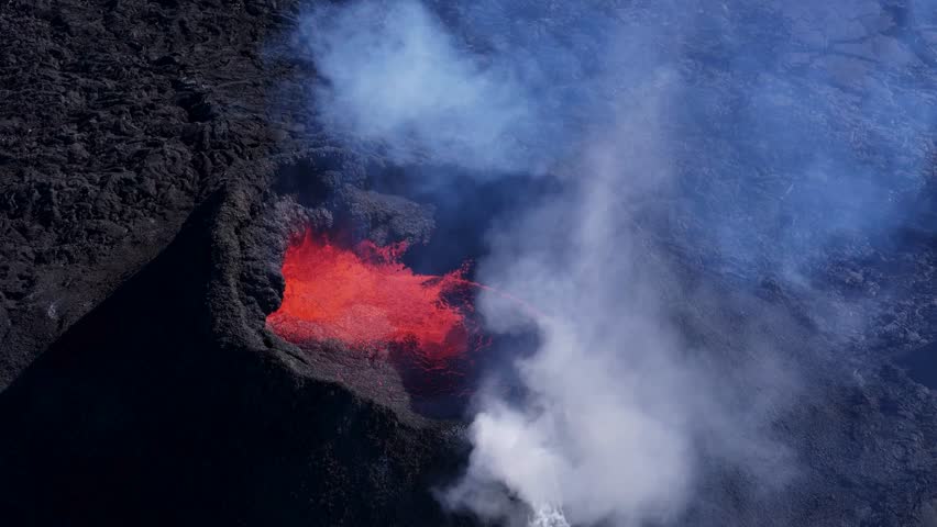 Powerful eruption in Hawaii Volcanoes National Park displaying bright orange lava flowing within the volcanic crater and a large plume of smoke rising around the dark landscape.