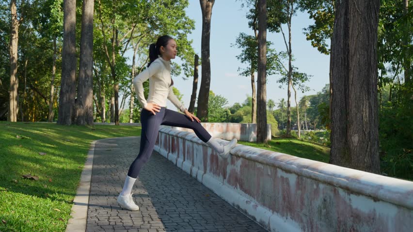 Young athletic woman warming up and stretching her leg muscles before a morning run in a sunny park