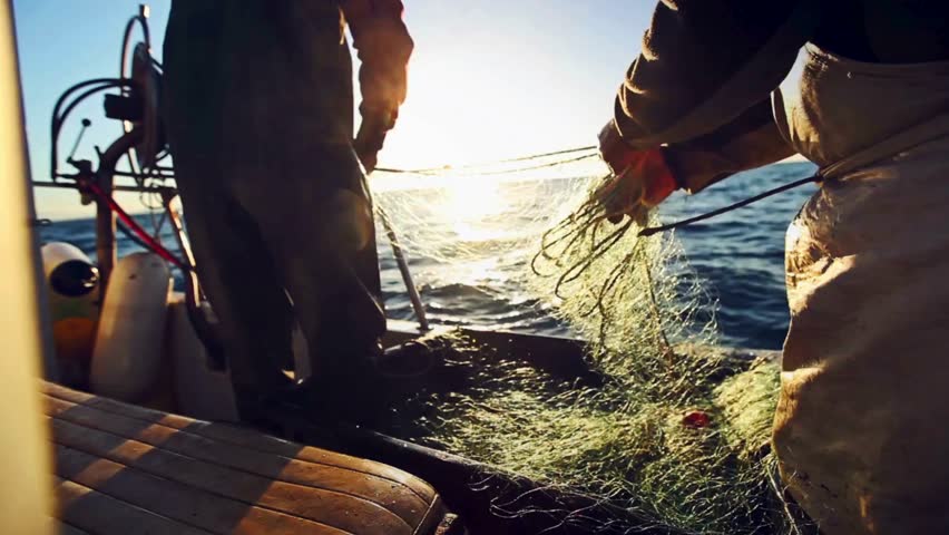 Fishermen skillfully cast and retrieve nets from a boat during golden sunset hours, capturing a serene moment of traditional fishing practices on the water.