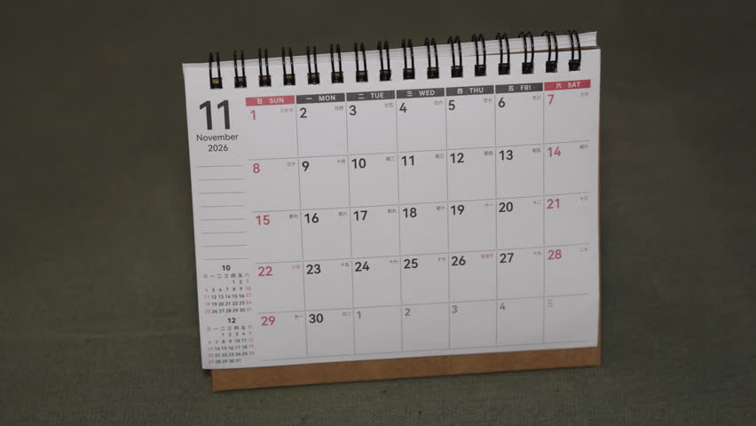 Wide close-up of a desk calendar as a hand flips the page from November 2026 to December 2026. Static camera captures a clear end of year month transition and planning concept on a work surface.