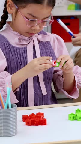 Focused child builds with interlocking math blocks while sitting at a white classroom table