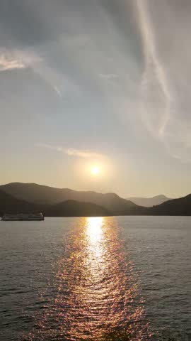 A ferry heads into port, passing through the rays of the setting sun reflecting off the water surface of Vancouver Bay on a summer day, British Columbia, Canada