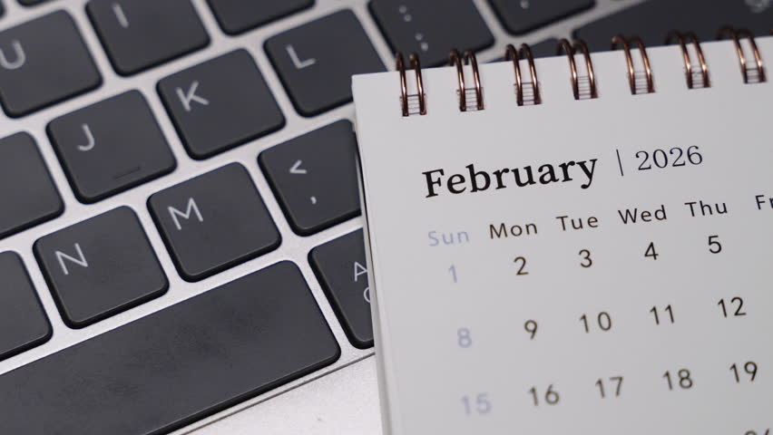 Close-up of a desk calendar showing February 2026 placed on a laptop keyboard. Camera slowly rotates to the right, revealing date layout and clean monthly planning concept in a modern workspace.