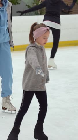 Girl skates trains doing exercises spin on ice rink. Figure skating coach works with child. Childrens sport. Vertical shot