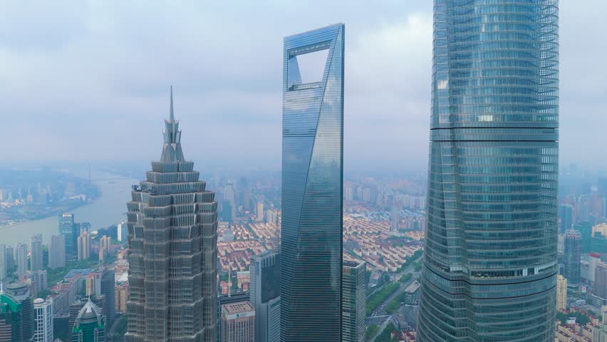 Aerial drone shot of the Shanghai Tower, Shanghai World Financial Center, and Jin Mao Tower rising above the crowded urban financial district in Shanghai, China.