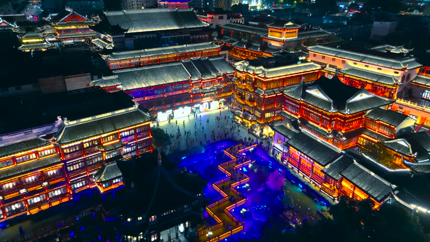 Aerial look at illuminated traditional Chinese architecture featuring pagodas and crowded courtyards late at night in Yu Garden, Shanghai, China.