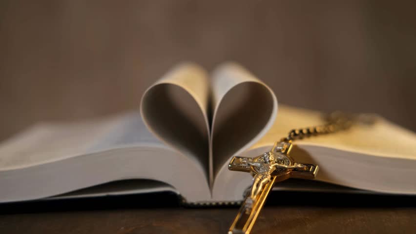 Heart-shaped pages of an open book showcase the beauty of literature, paired with a crucifix, representing love, faith, and spirituality. Ideal for meaningful imagery.
