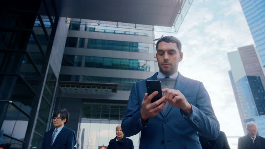 Businessman Activates AI Smartphone While Walking through City Business Center. Hologram Code and Network Symbols Illustrate Wireless Data Flow, Digital Banking, Cloud Services, Secure Messaging