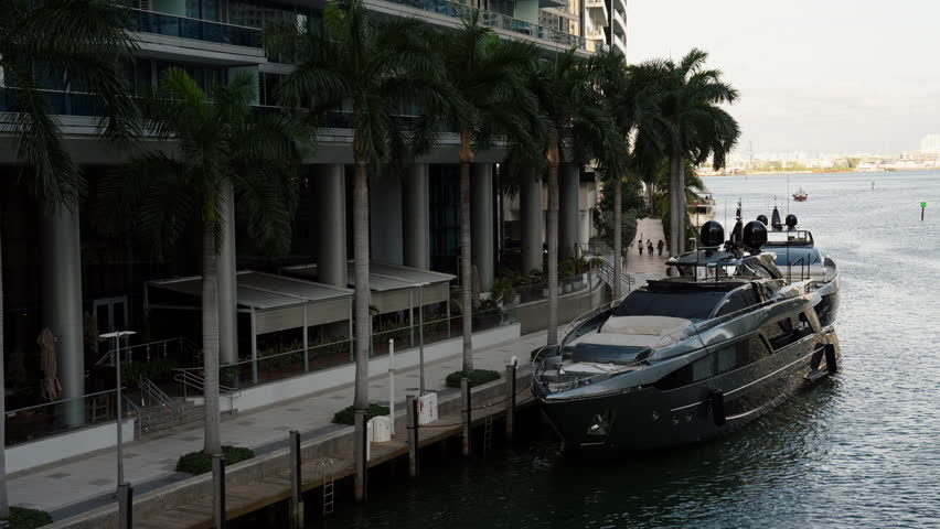 Luxury yacht moored beside a modern waterfront promenade with palm trees, upscale residences, and calm bay water, capturing an exclusive coastal lifestyle in Miami.
