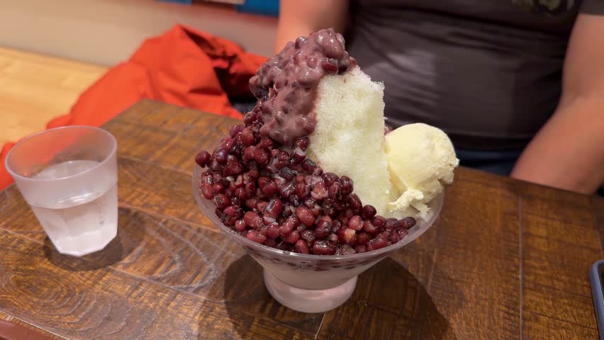 Delicious Japanese kakigori dessert with red bean and ice cream served in a bowl on a wooden table