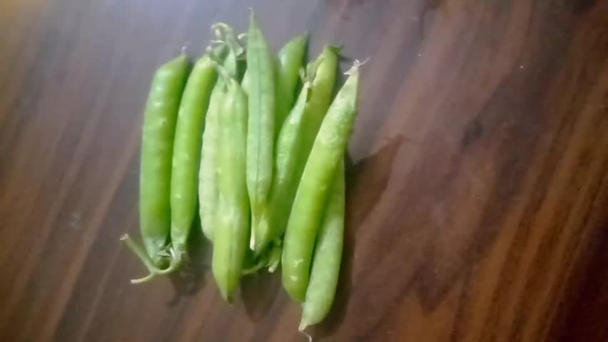 Fresh green peas in pods placed on a wooden surface. Healthy organic vegetable, natural food ingredient, close-up view for agriculture and nutrition concepts.