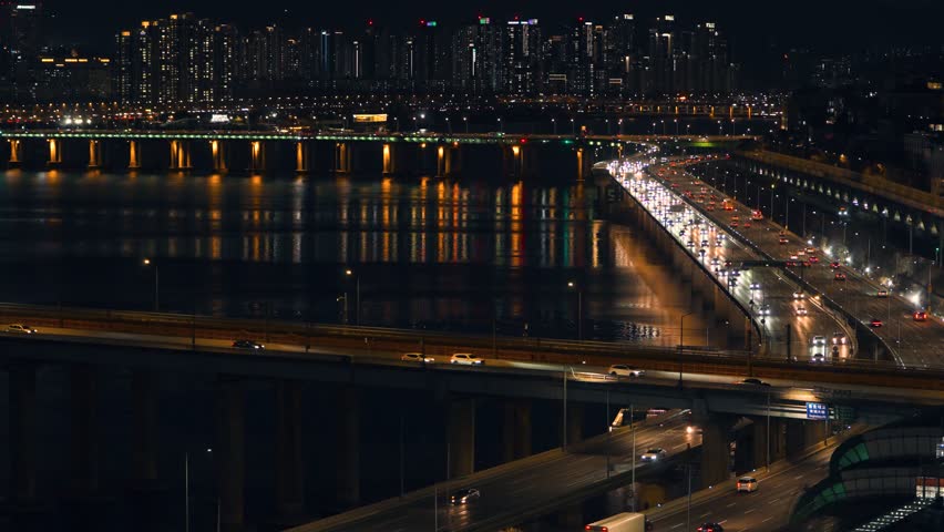 Static high-angle view of two Line 3 subway trains passing each other on the Dongho Bridge while cars travel on the Gangbyeonbuk-ro expressway against the Seoul night skyline