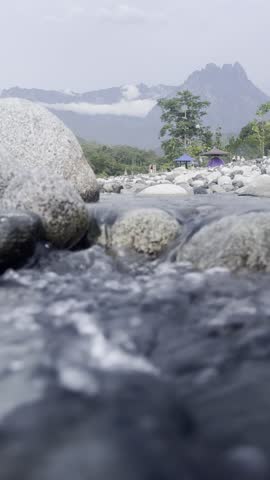 Close up view of mountain stream river rocks with blurred campsite and mountain peak scenery in Sabah Borneo.