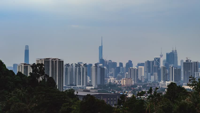Timelapse of dense Kuala Lumpur skyline, featuring Merdeka 118, the Petronas Twin Towers, and the KL Tower under a hazy sky.