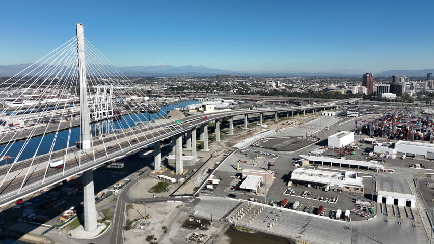 Wide aerial view of Terminal Island and the International Gateway Bridge in Long Beach, CA featuring shipping containers, 18-wheelers in motion, and major port infrastructure.