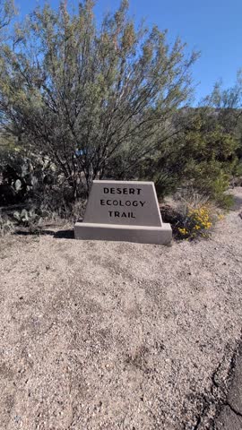 Slow pan in on Desert Ecology Trail sign surrounded by desert plants and gravel landscape inside Saguaro National Park in southern Arizona.