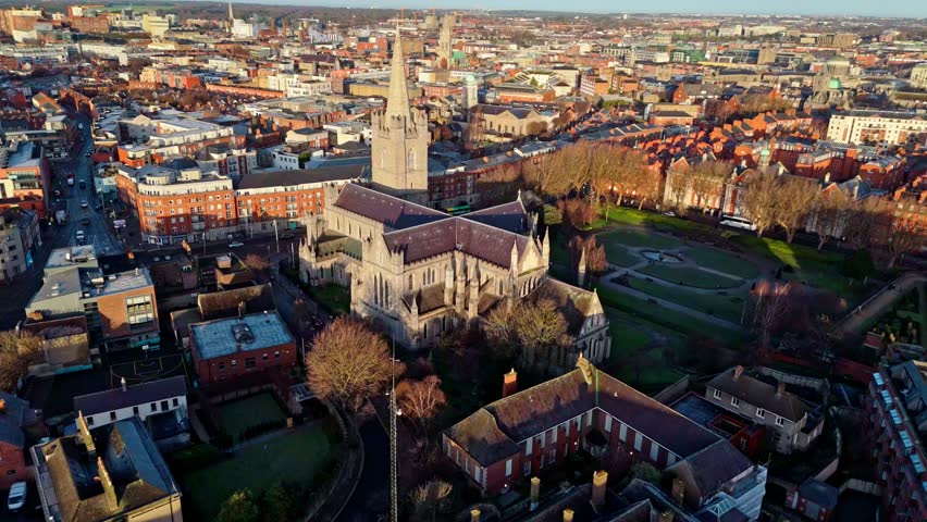 Aerial drone shot of the St Patricks Cathedral ion the capital of Ireland, Dublin. Shot at a golden winter sunrise with the park in view with its grass and trees. Glowing Irish architecture and city