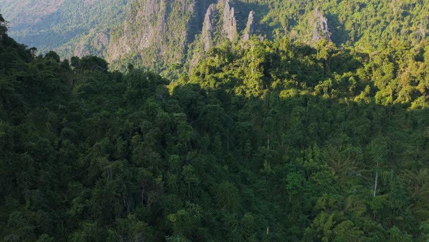 Paraglider flies over Laos mountains at sunset with a warm orange sky and silhouette of hills shot from a unique aerial perspective