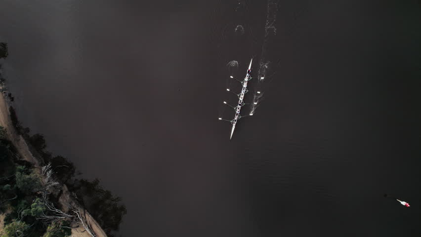 Top view of rowers move smoothly through the water in a boat on a river during early morning hours