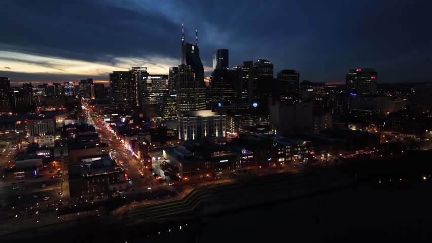 Aerial night panorama of downtown Nashville with illuminated streets, glowing skyscrapers and city lights stretching across skyline under dramatic evening sky. Panorama wide shot.