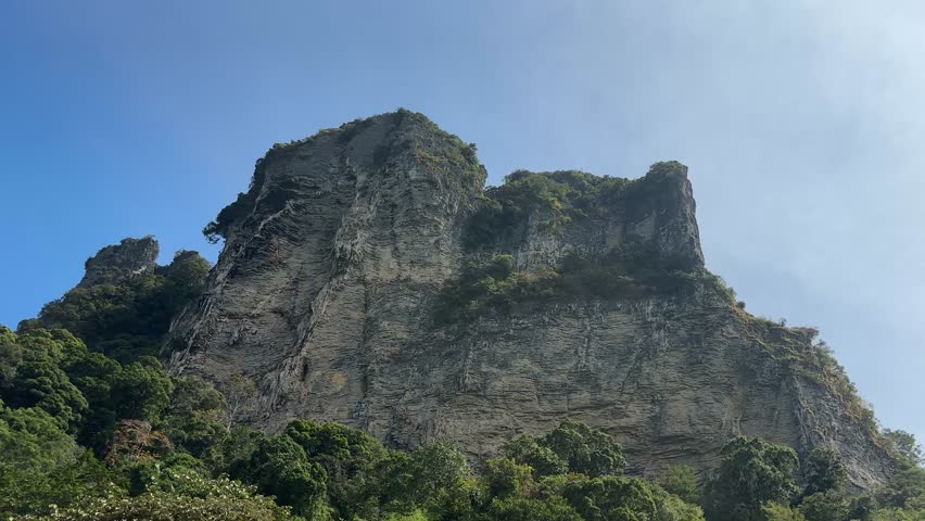 Massive limestone cliff rising above tropical forest near Ao Nang area, dramatic rock formation and natural landscape in Krabi region Thailand, popular travel destination