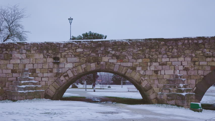 Ancient Roman Stone Bridge in Winter, Salamanca Spain, with Snow-Covered Arch and Steps at Dawn