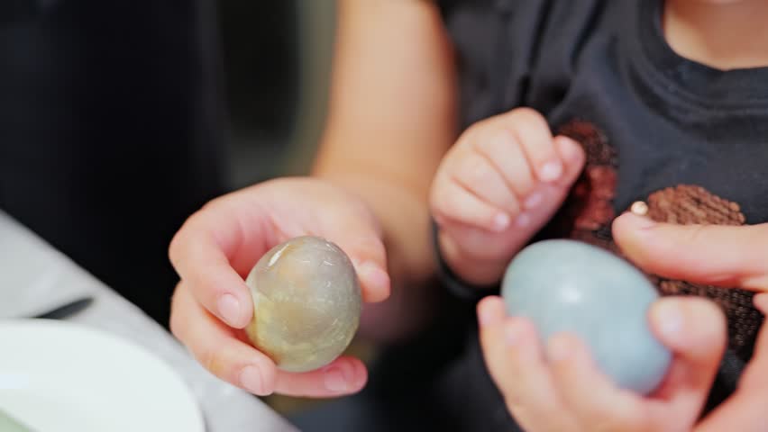 Close-up shows toddler hands playfully cracking eggs during curious kitchen play