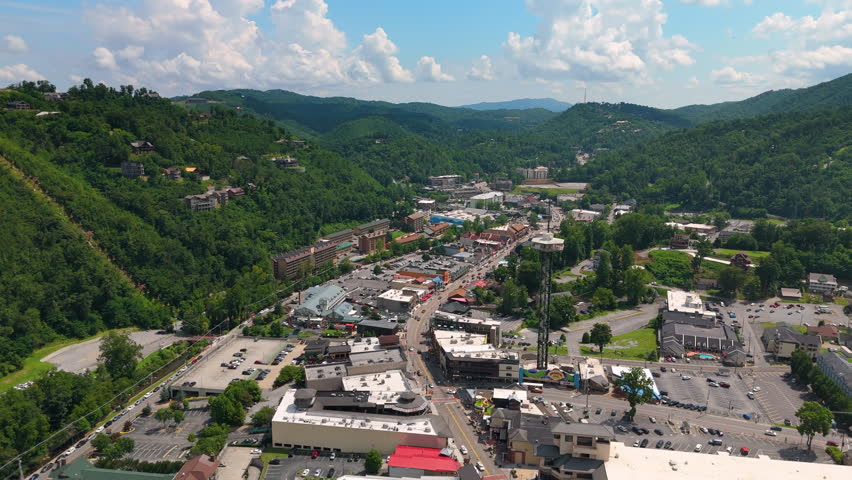 Aerial panorama of Gatlinburg, Tennessee with bustling main street filled with shops and attractions, observation tower and Smoky Mountains National Park nearby.