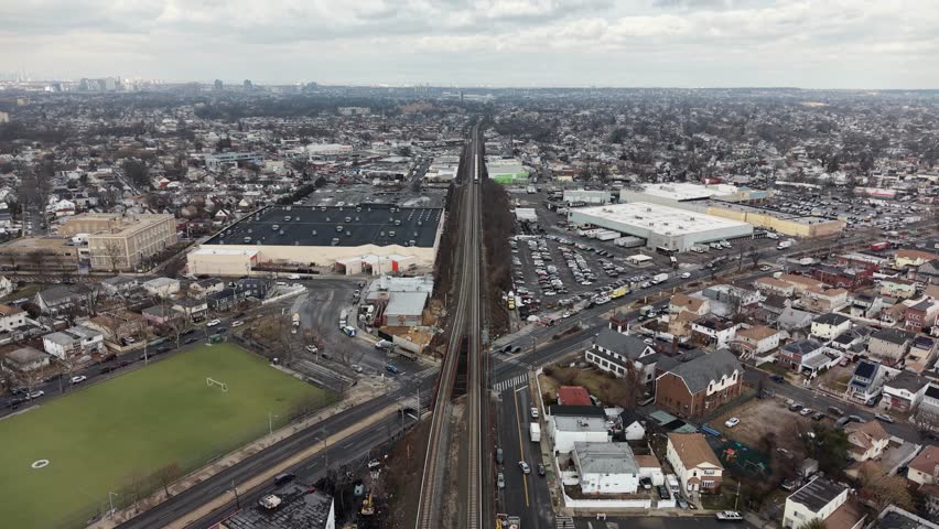 Queens new york high angle drone view of suburban cityscape bisected by long railroad tracks, industrial and residential areas under cloudy sky