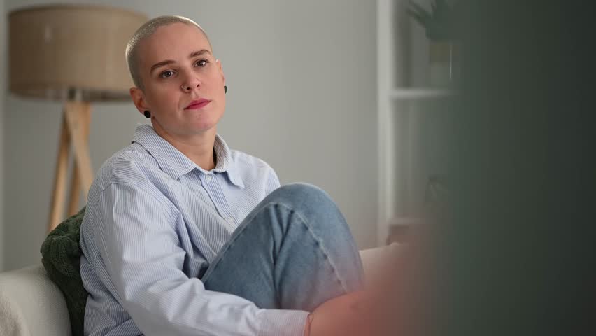Young woman with shaved head talking about her problems and mental health during a psychotherapy session with her psychologist in the office