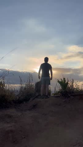 Rear view of a man standing with arms outstretched on a mountain peak at sunrise