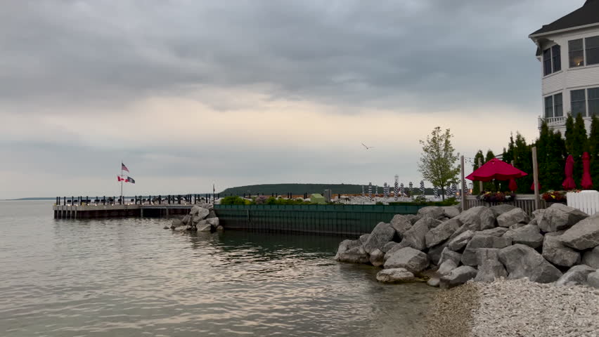 Rocky Lake Huron Coastline with Island Architecture. Static view of the historic Mackinac Island, Michigan shoreline featuring clear lake water and coastal buildings on a bright summer evening. Seagulls fly overhead.
