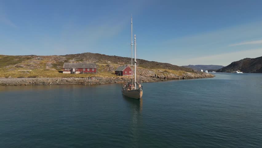 Sailing boat anchored in a Greenland fjord near red houses