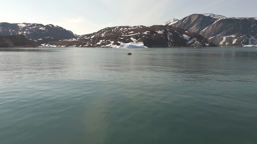 Yellow boat sailing among icebergs in Greenland fjord