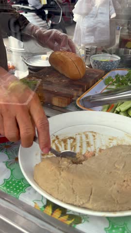 Local street food vendor preparing banh mi sandwich at market stall in Ho Chi Minh City, capturing authentic daily life, Vietnamese food culture, and traditional street food in Vietnam.