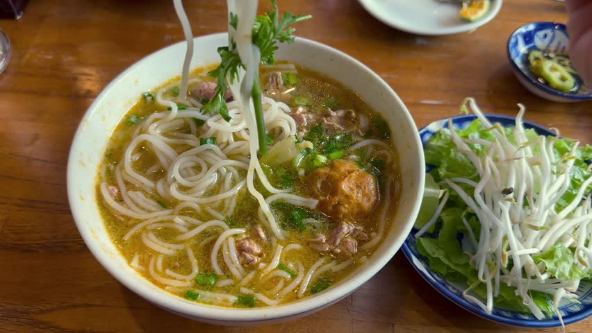 Close-up of traditional pho noodle soup eaten with chopsticks, capturing authentic Vietnamese food culture, daily life, and local dining experience in Vietnam.