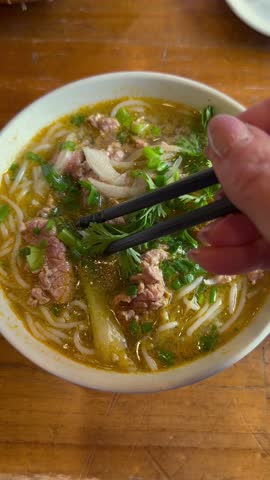 Close-up of traditional pho noodle soup eaten with chopsticks, capturing authentic Vietnamese food culture, daily life, and local dining experience in Vietnam.