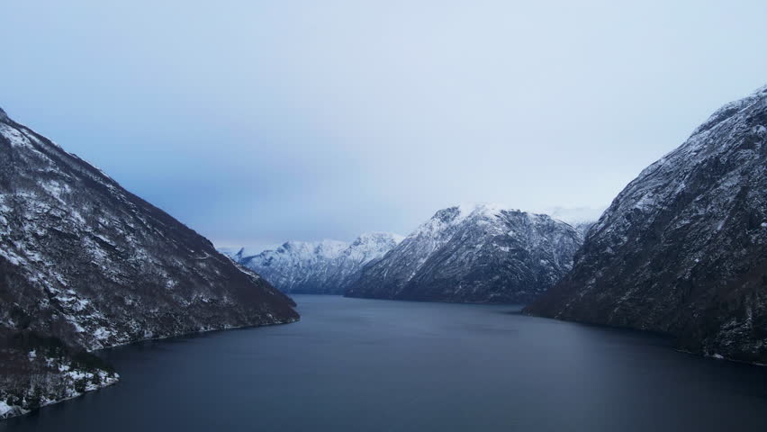 Scenic drone shot of Sunnylsfjord, a fjord in Norway with tall mountains and steep cliffs and snow is covering the landscape on a bright winter day in Norway