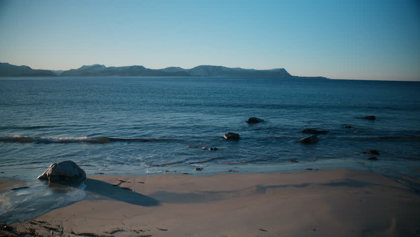 Scenic shot of waves coming in to the beach with mountains in the horizon on a cold bright winter day in Norway