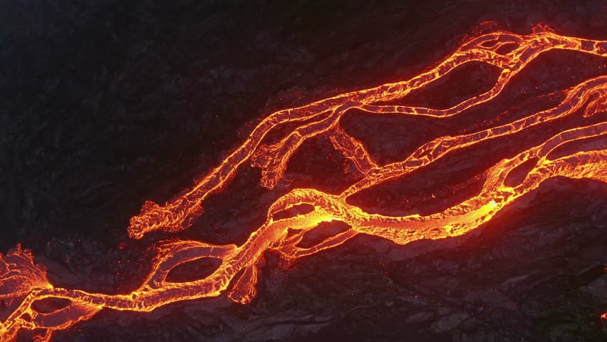 Aerial view of bright orange lava rivers moving across dark hardened lava fields. Hot molten rock flows, cooling to black stone in Hawaii Volcanoes National Park.