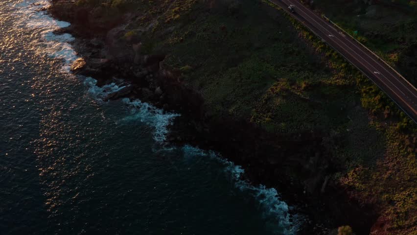 aerial coastal road with green hills ocean cliffs moving cars and golden sunrise lighting
