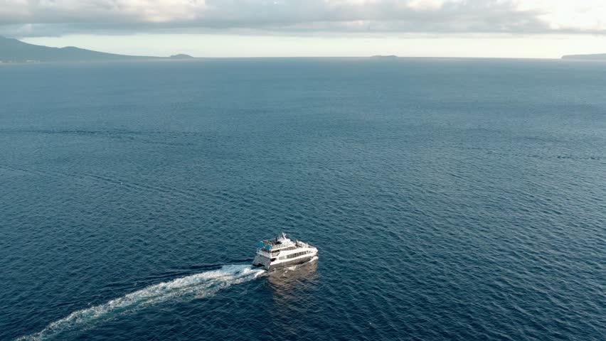 Static aerial shot white boat sailing across blue ocean with distant island and calm water