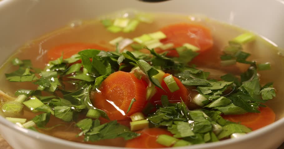 Chicken broth is stirred with a spoon and taken. Homemade organic chicken broth.