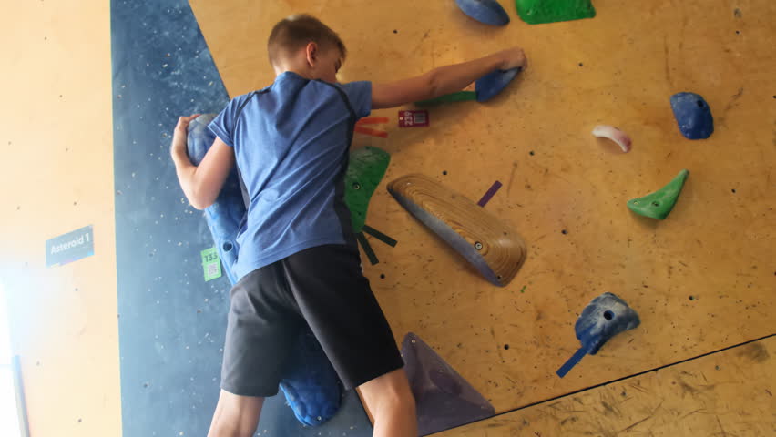 Small boy discovers new activity climbing on artificial wall at gym. Child holds grip passing route during bouldering session slow motion