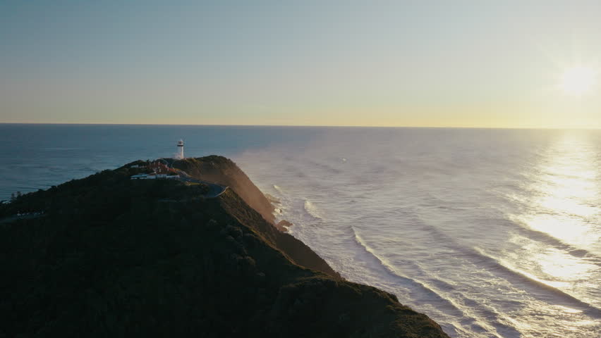 Clifftop of Byron Bay as sunlight shimmers across rolling ocean at dawn
