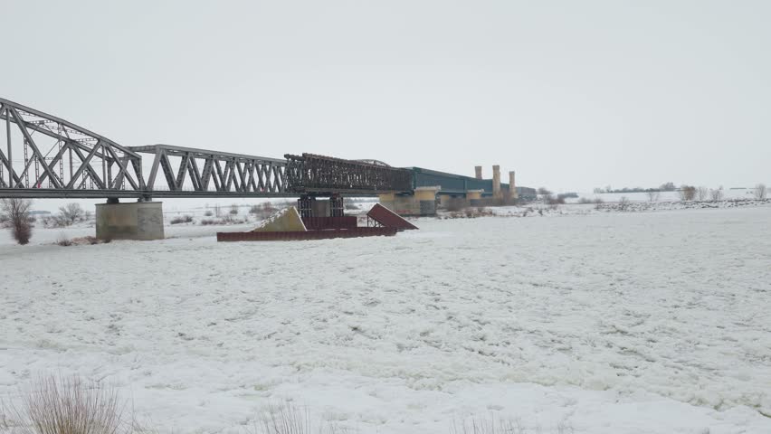 Historic railway bridge in Tczew spanning frozen Vistula river during winter. Snow covered landscape stretching across Poland while icy water forming natural patterns. Cold season scenery combining