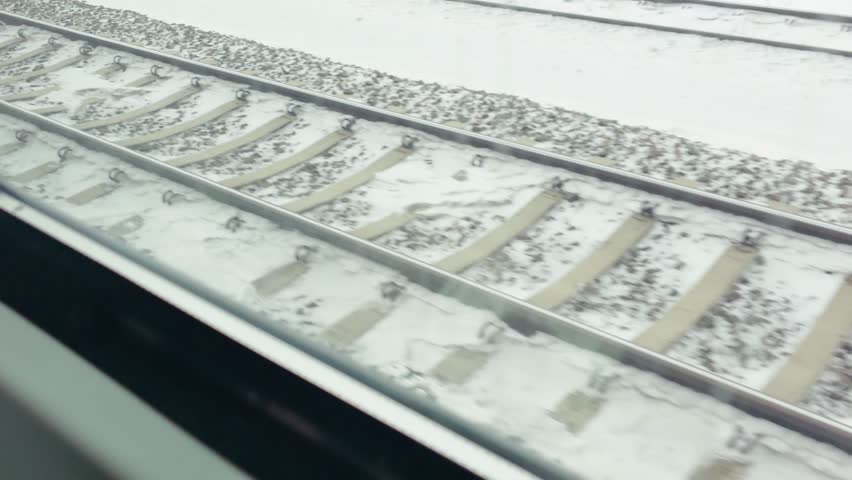 Railway tracks covered with snow passing by window during train travel. Winter journey continuing across frozen landscape with steel rails and sleepers. Public transport moving through cold weather