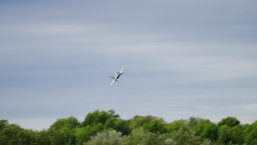 An Hornet fighter jet performs a high-speed aerial maneuver, flying directly towards and over the camera against a cloudy grey sky. Shows power, speed, and military technology.