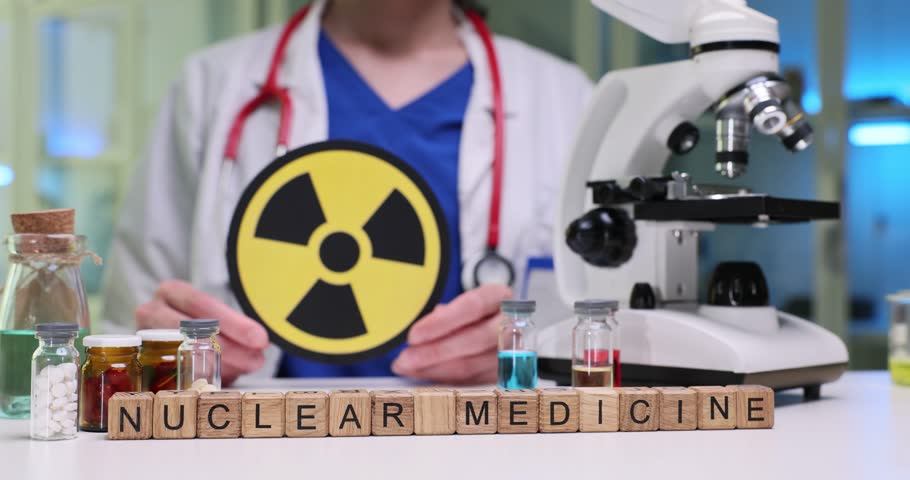 Doctor shows radiation warning sign to emphasize potential exposure risks in medical environment. Wooden cubes on table form phrase Nuclear Medicine